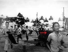 Historical photograph of people running along a Hilo street; a red arrow already on the supplied image points toward a young man at right.